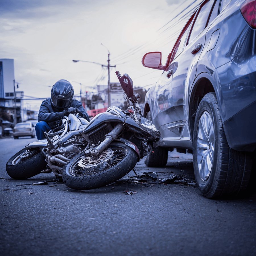 Motorcycle collision aftermath with rider resting beside the damaged bike and car